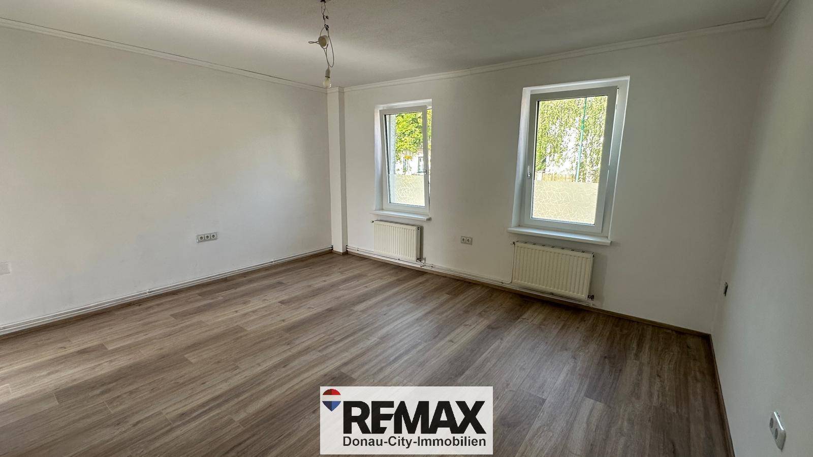 Geräumiges, helles Zimmer mit zwei Fenstern und Laminatboden, ideal als Wohn- oder Schlafbereich.