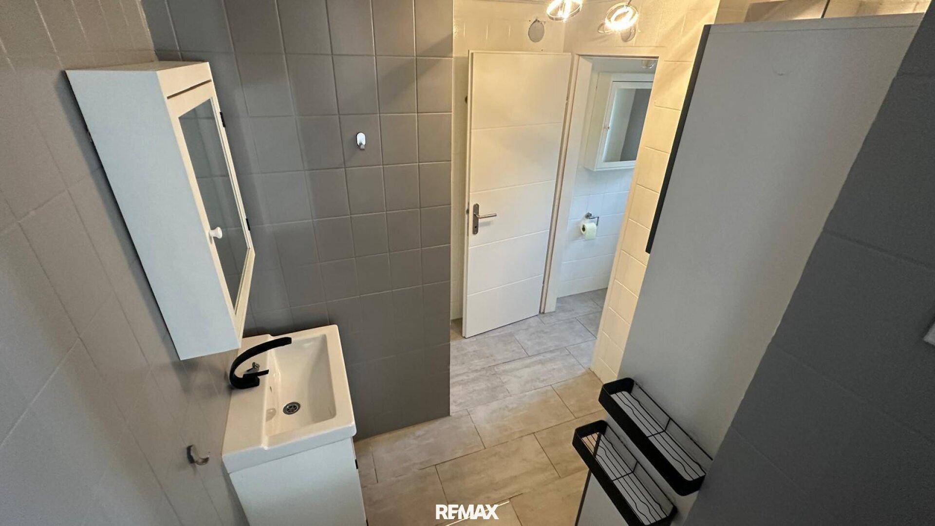 Modernes Badezimmer mit Waschbecken, Spiegelschrank und grauen Fliesen.