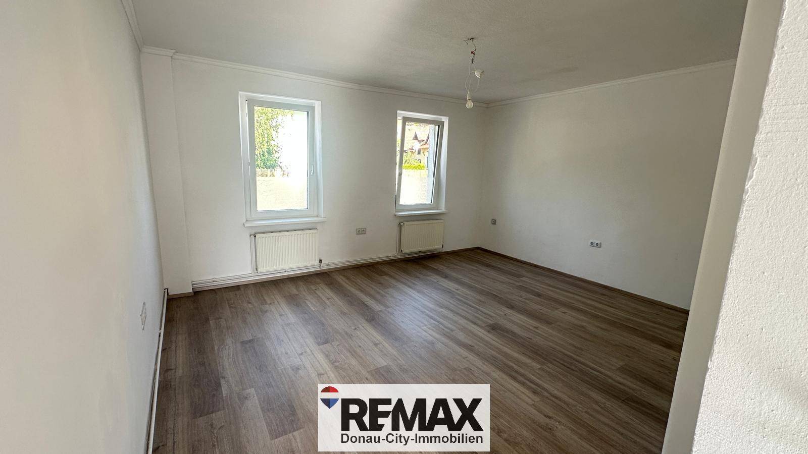 Geräumiges, helles Zimmer mit zwei großen Fenstern und modernem Laminatboden.