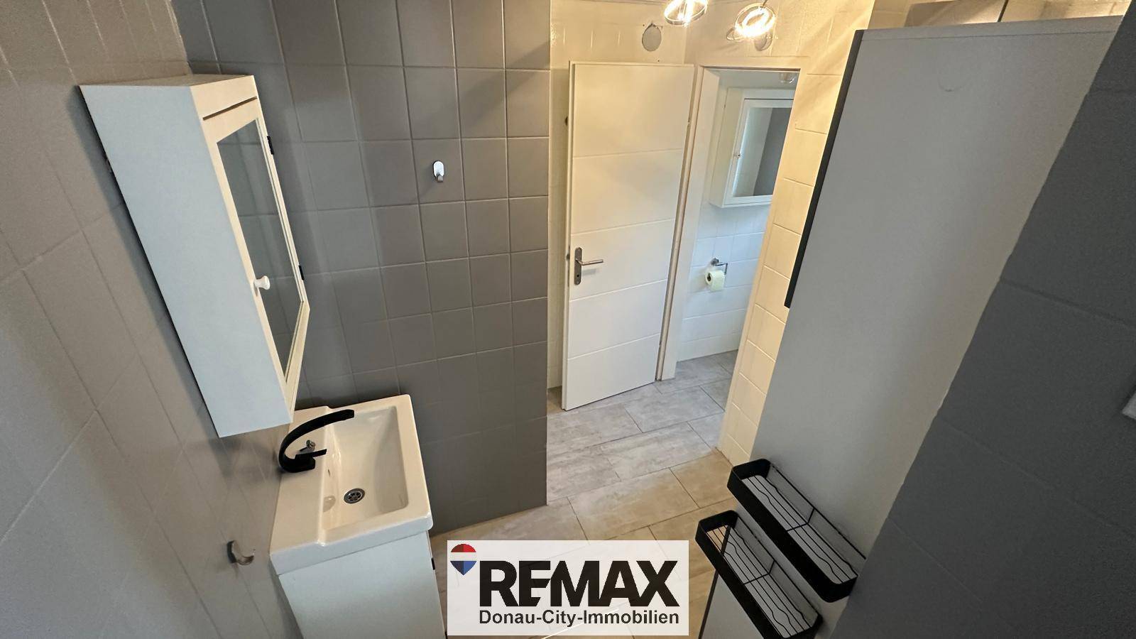 Modernes Badezimmer mit Waschbecken, Spiegelschrank und grauen Fliesen an den Wänden.