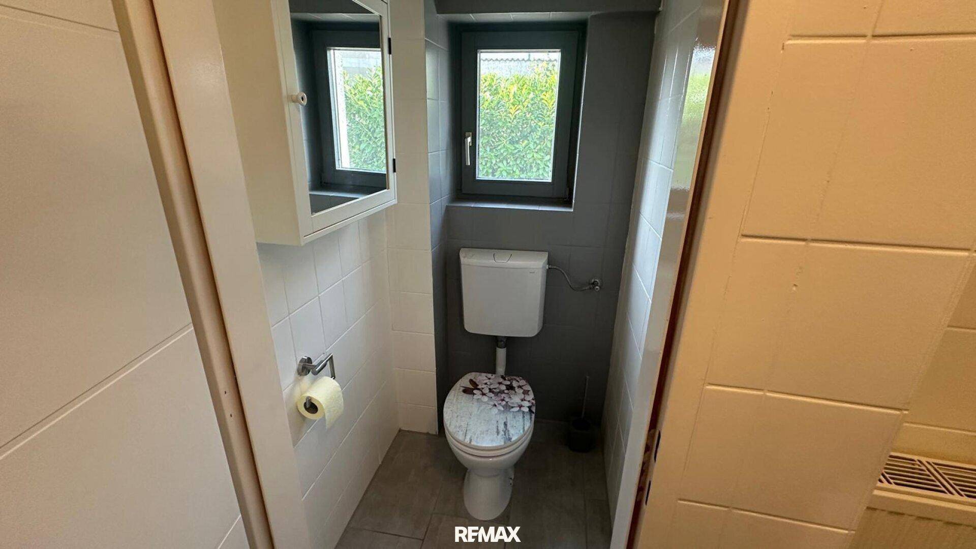 Kleines Gäste-WC mit Fenster, Wand-WC und Spiegelschrank.