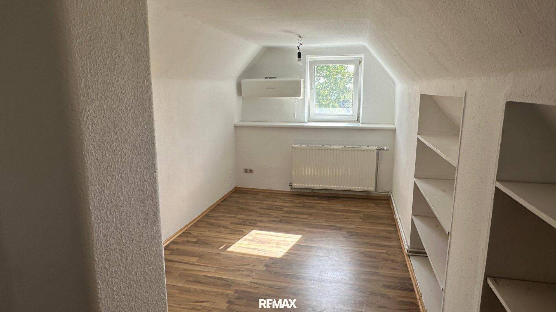 Kleiner Raum im Dachgeschoss mit Schrägdecke, Laminatboden, Fenster und integrierten Regalen.