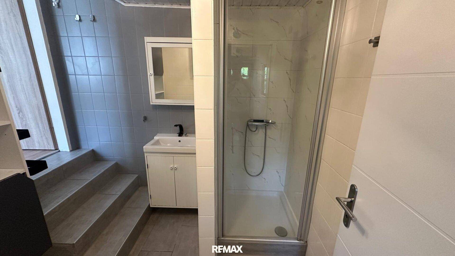 Modernes Badezimmer mit Duschkabine, Waschbecken und grauen Fliesen.