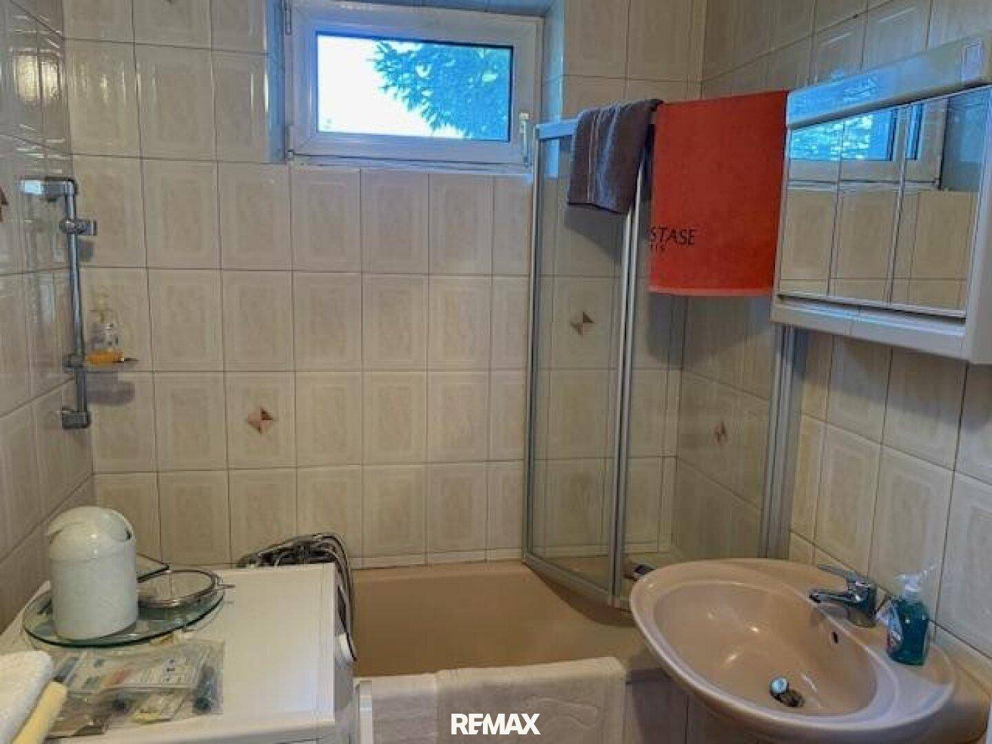 Badezimmer mit Dusche, Waschbecken und Fenster, gefliest in hellen Farben.