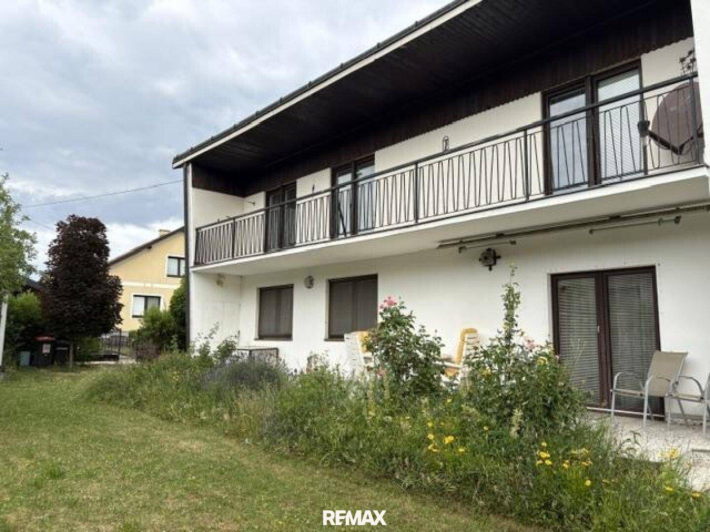 Hinteransicht des Hauses mit Terrasse, Gartenmöbeln und üppiger Vegetation.