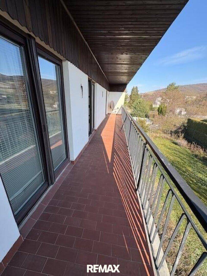 Langer Balkon mit Fliesenboden und Metallgeländer mit Blick ins Grüne.