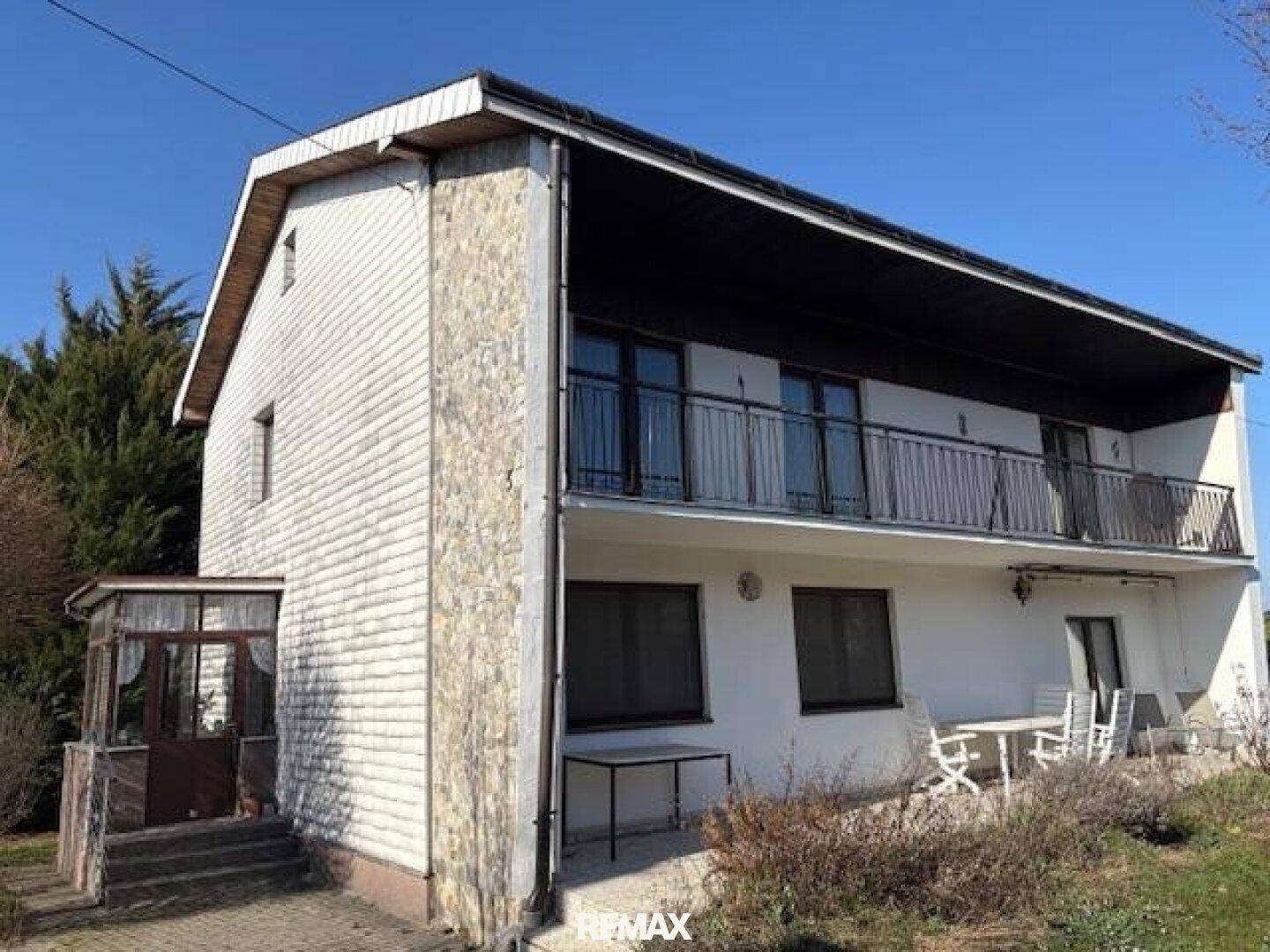 Ansicht des Hauses mit Balkon und Terrasse im Freien unter klarem Himmel.