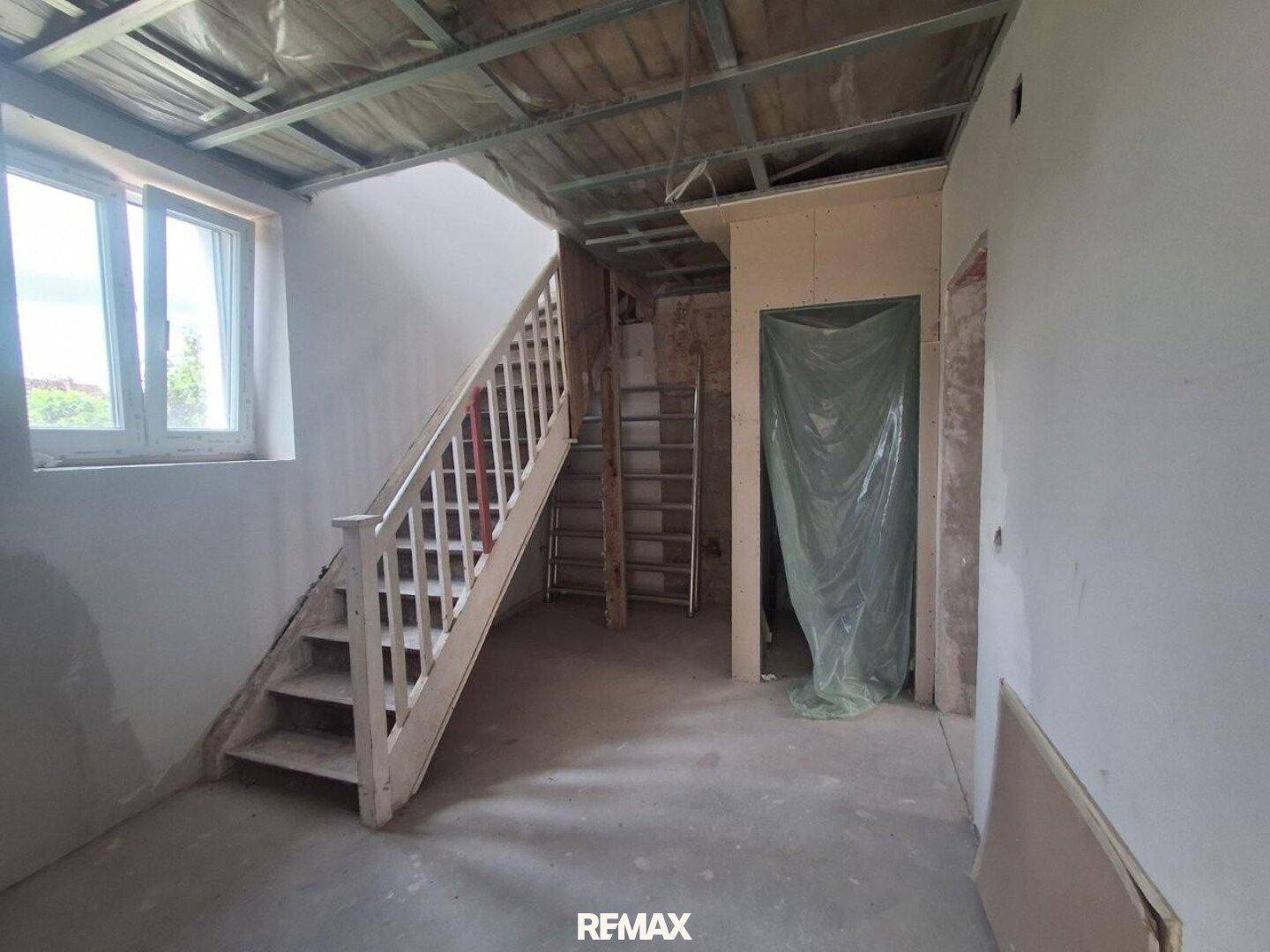 Treppenhaus im Rohbau mit Holztreppe und Fenstern, bereit für den weiteren Innenausbau.