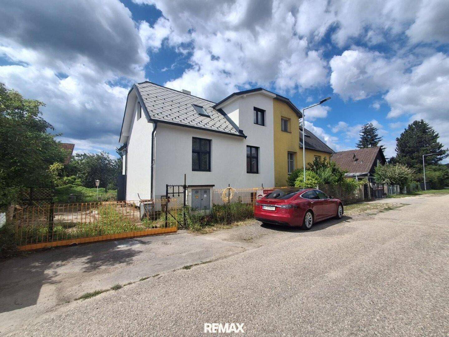 Vorderansicht des Hauses mit weißer Fassade und neuem Dach, ein rotes Auto parkt an der Straße.