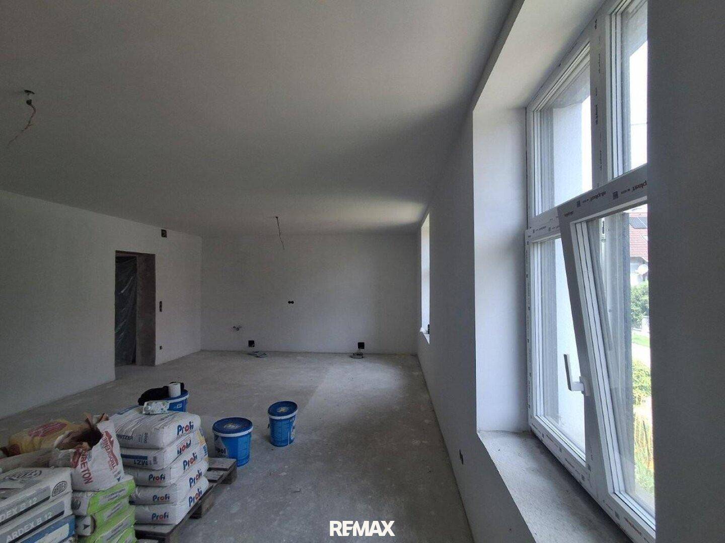 Großer, heller Raum im Rohbau mit weiten Fenstern und Baumaterialien, bereit für den Innenausbau.