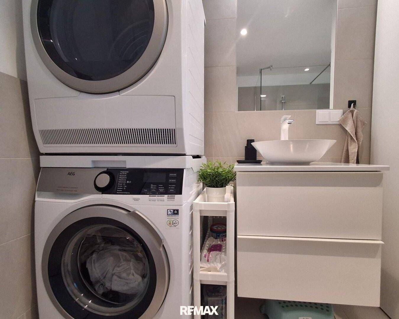 Detailansicht des Badezimmers mit Waschmaschine, Trockner und modernem Waschtisch mit Spiegel.
