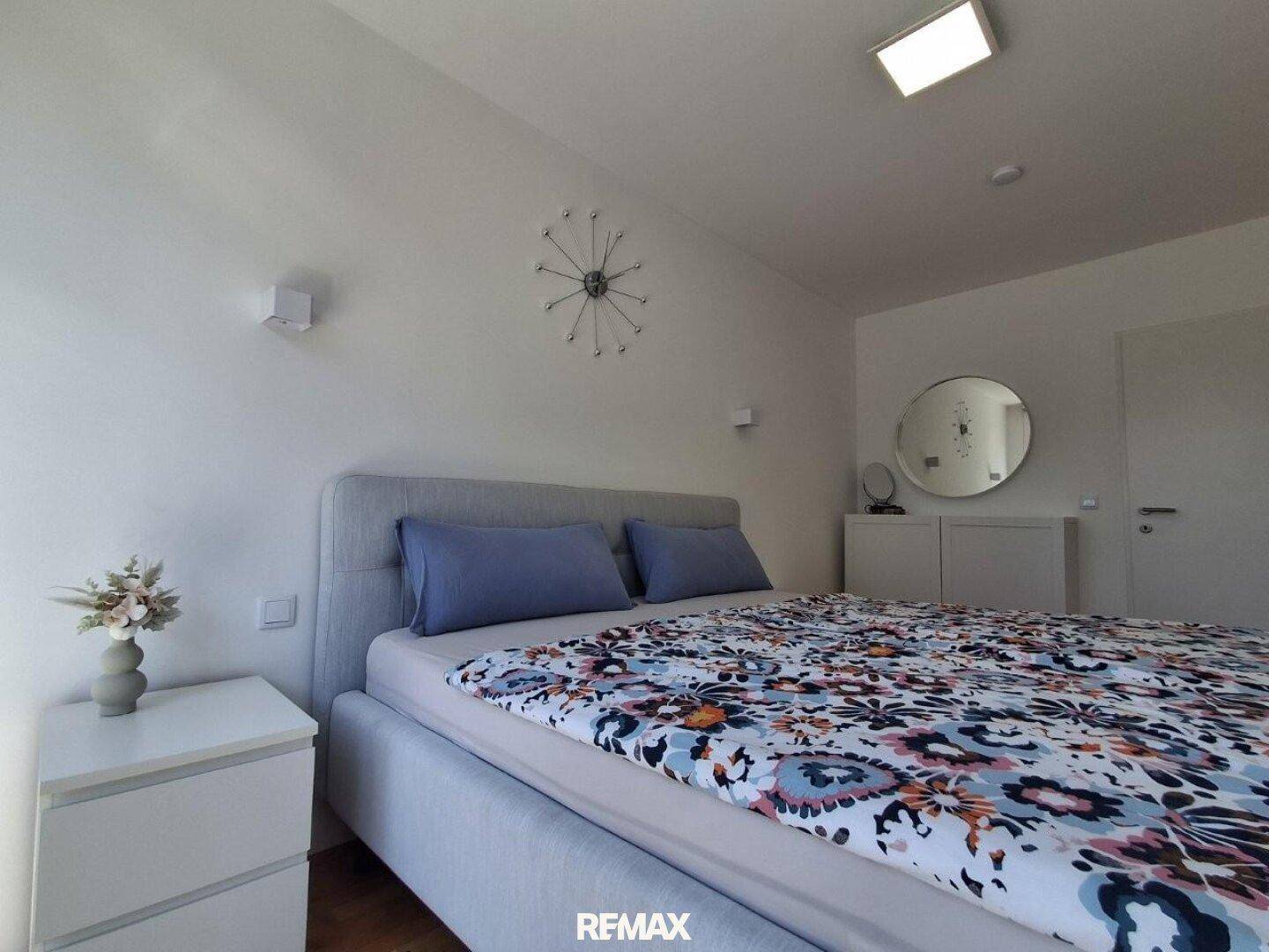 Schlafzimmer mit bequemem Bett, Nachttisch und dekorativem Spiegel, hell und freundlich gestaltet.