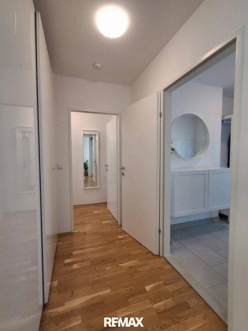 Heller Flur mit Holzfußboden und weißen Wänden, der zu den verschiedenen Räumen führt.