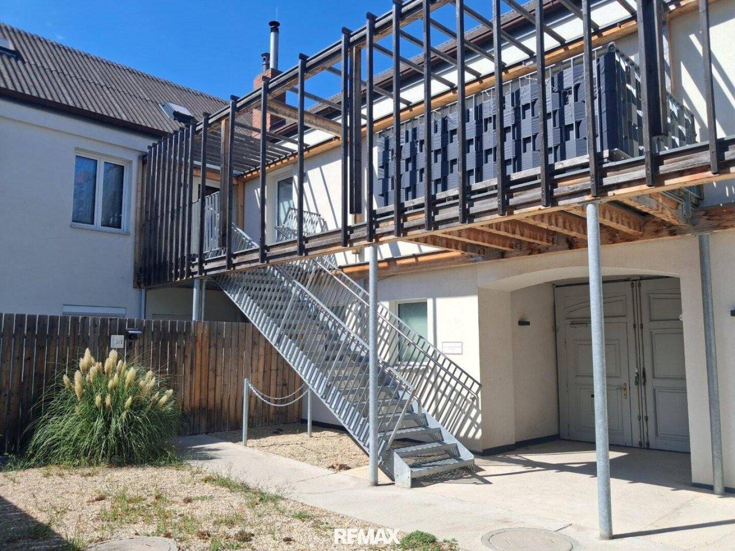 Außenansicht eines Gebäudes mit externer Metalltreppe und Holzverkleidung, die zu den oberen Etagen führt.
