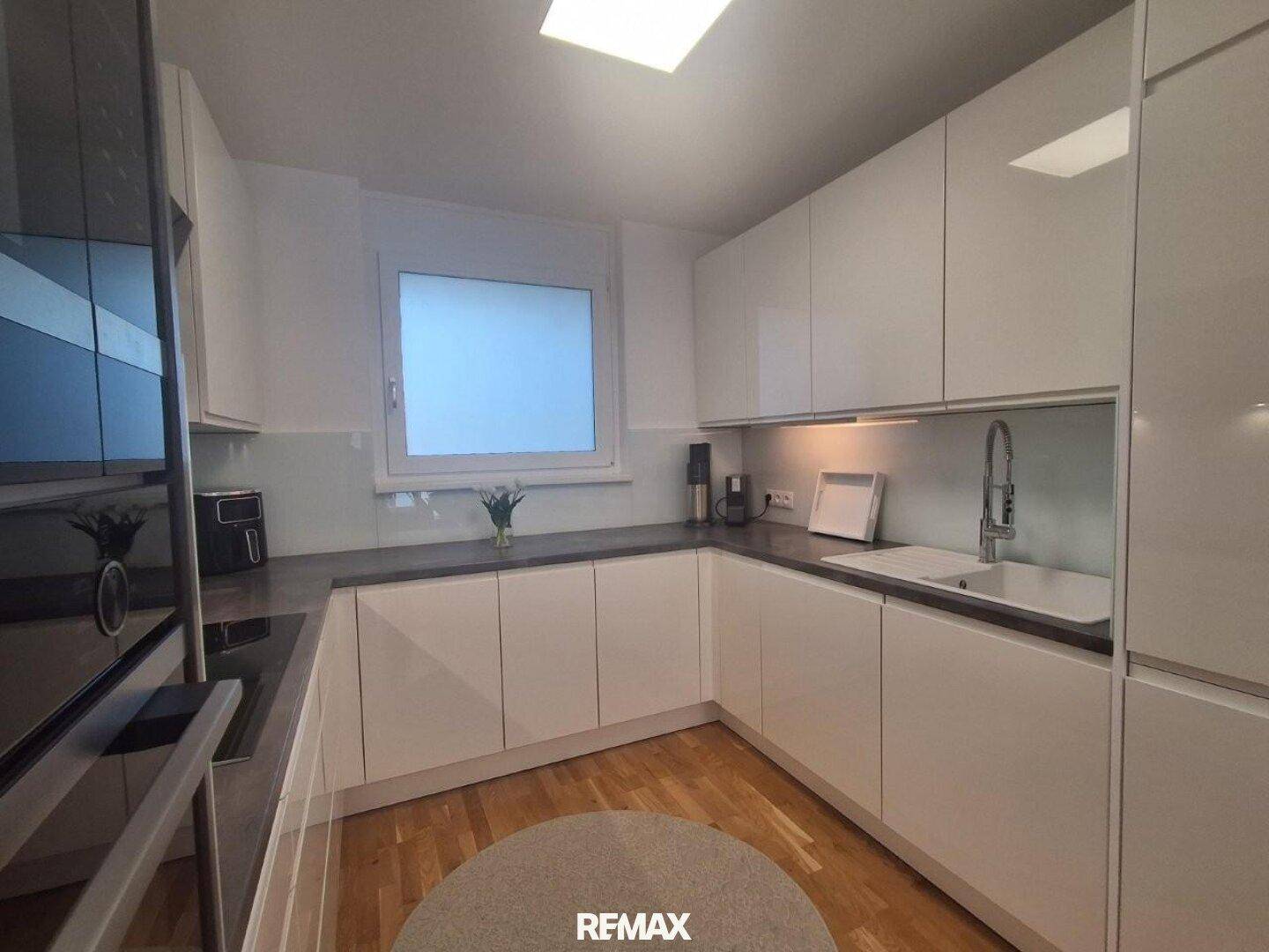 Moderne Einbauküche mit weißen Hochglanzschränken, dunkler Arbeitsplatte und Fenster für Tageslicht.