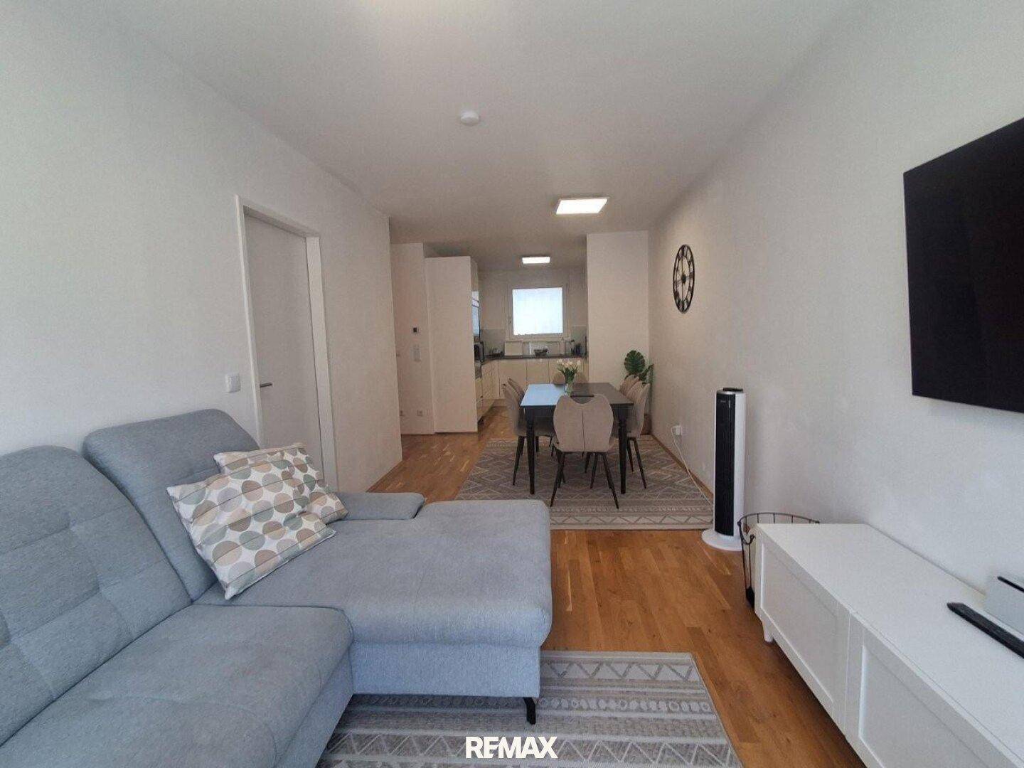 Geräumiger offener Wohn-Ess-Küchenbereich mit modernem Sofa und Esstisch, ideal für geselliges Beisammensein.