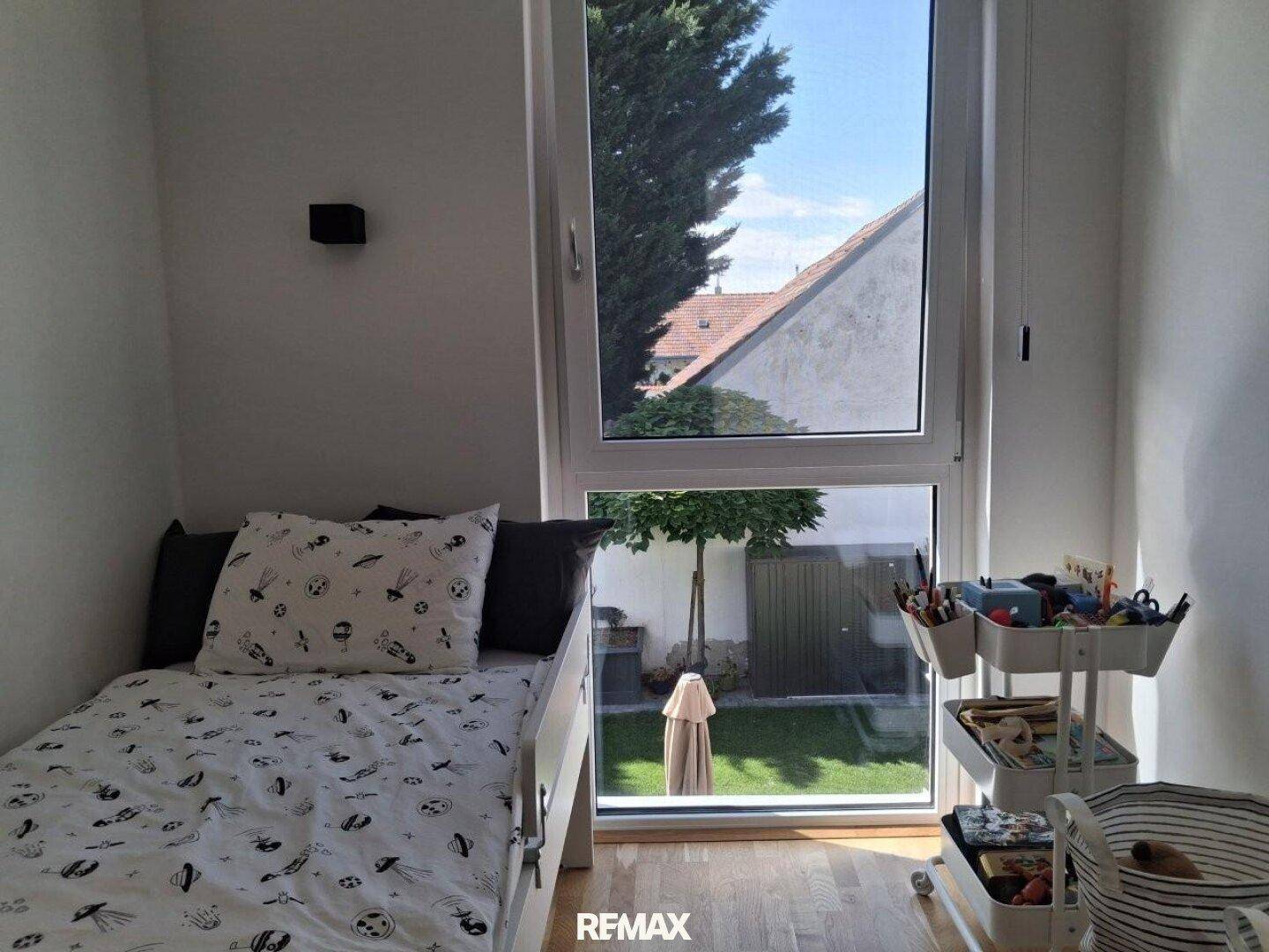 Kinderzimmer mit Einzelbett und großem Fenster, das viel Licht und einen Blick ins Grüne bietet.