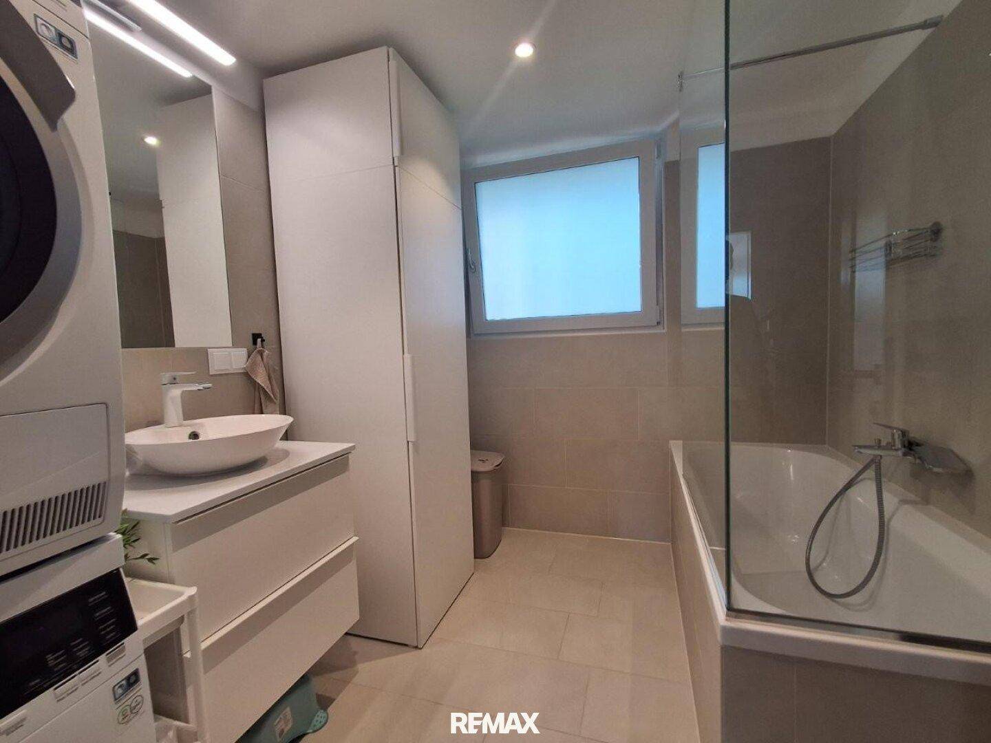Helles Badezimmer mit Badewanne, modernem Waschbecken und praktischem Waschmaschinen-Trockner-Turm.