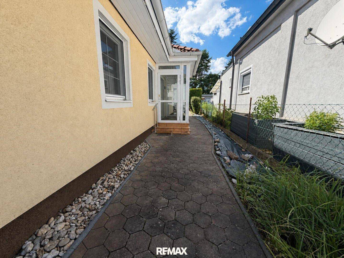 Schmaler gepflasterter Weg entlang der Hausseite, führt zum hinteren Gartenbereich.