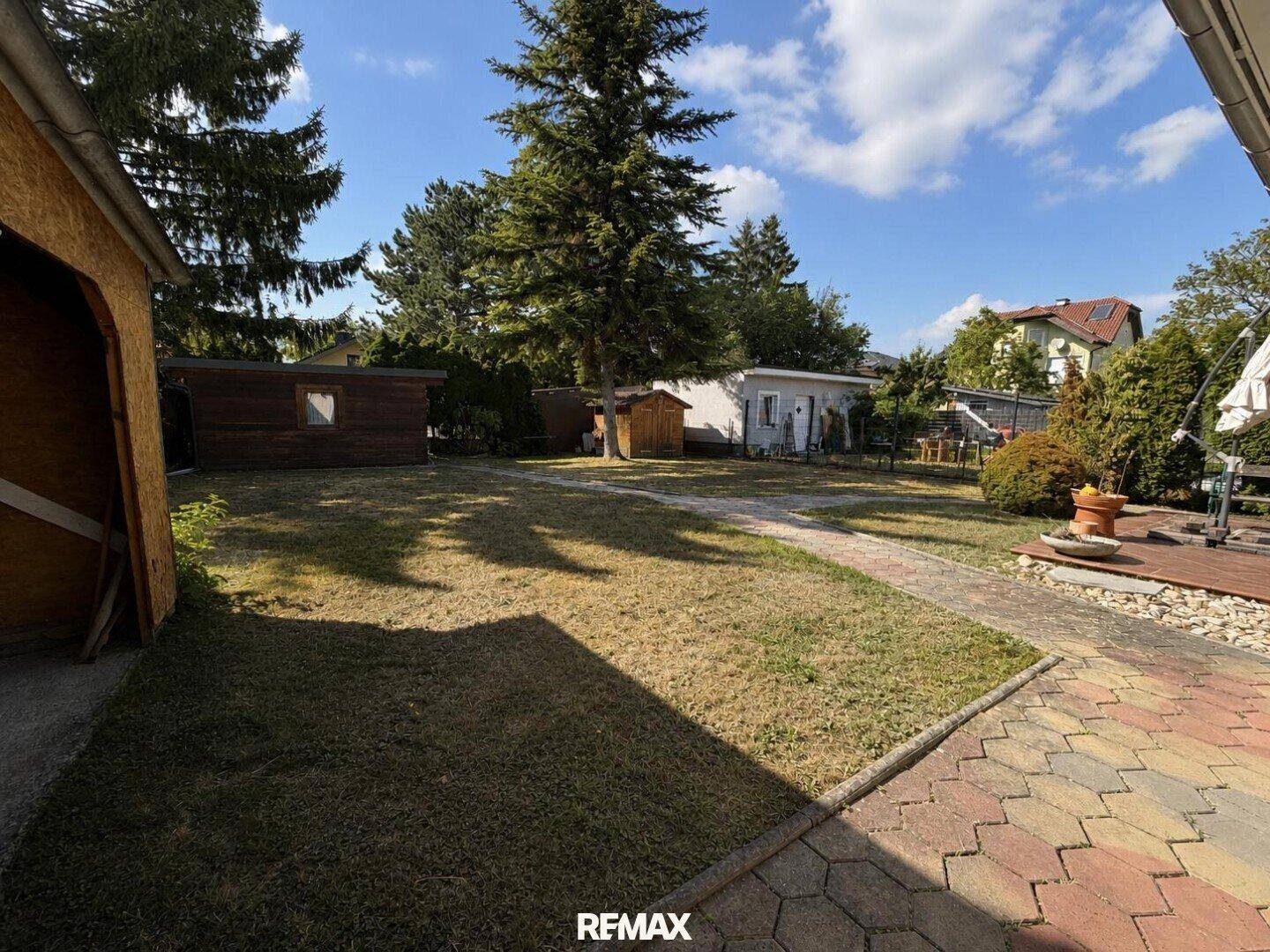 Großer Gartenbereich mit Rasenfläche und mehreren Gartenhäusern im Hintergrund.