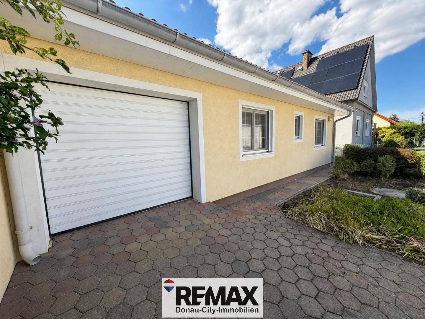 Garagentor und gepflasterte Einfahrt des Hauses, umgeben von Grünflächen.