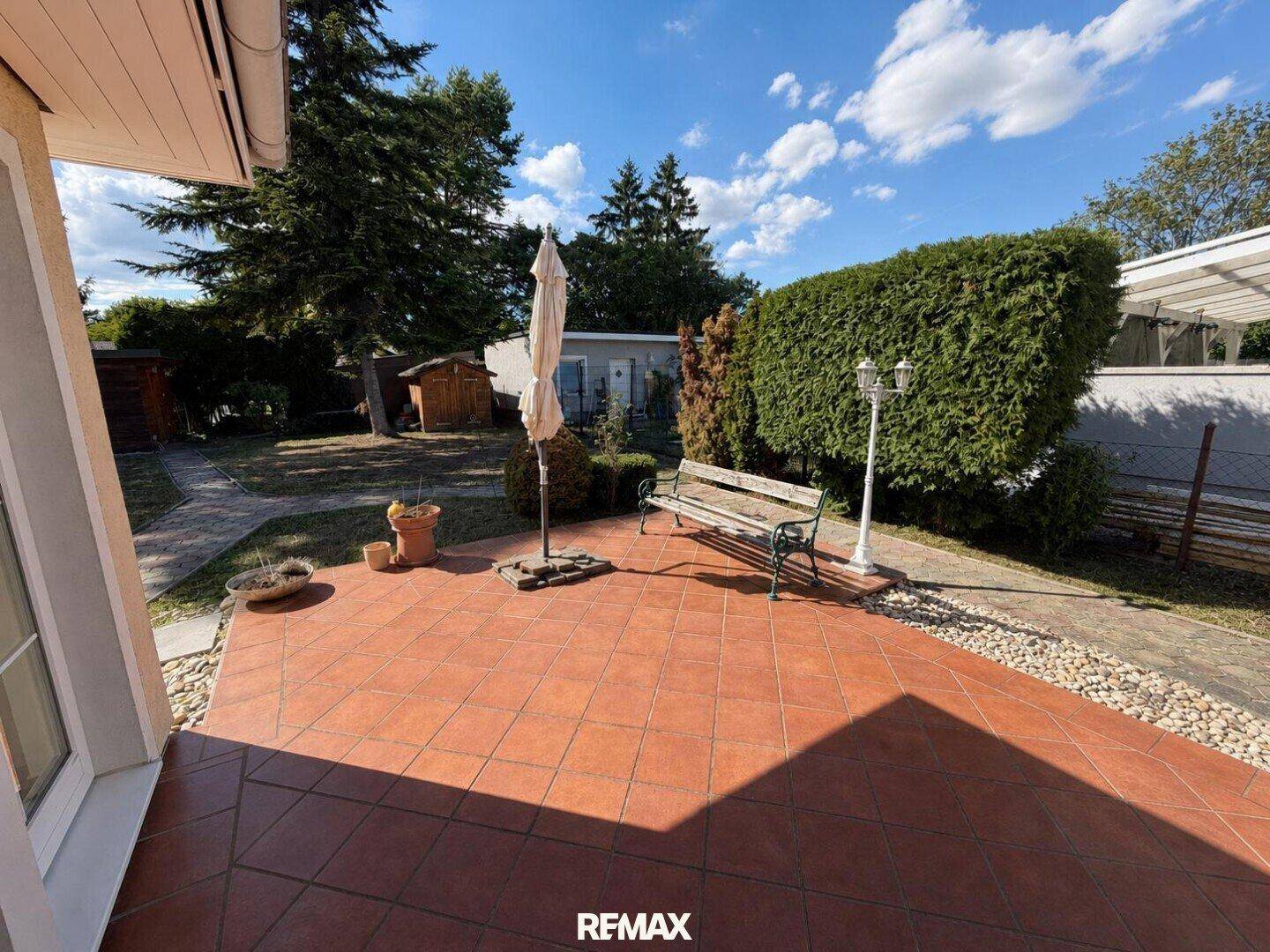 Gemütliche Terrasse mit Fliesenboden und Gartenbank, umgeben von gepflegten Hecken.