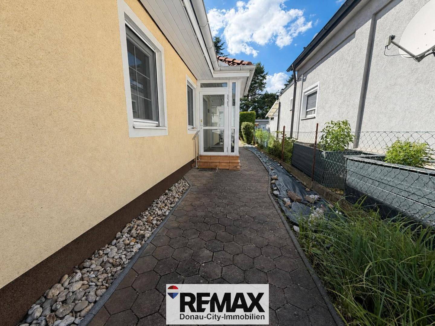 Schmaler gepflasterter Weg entlang der Hausseite mit Kiesstreifen und Pflanzen.