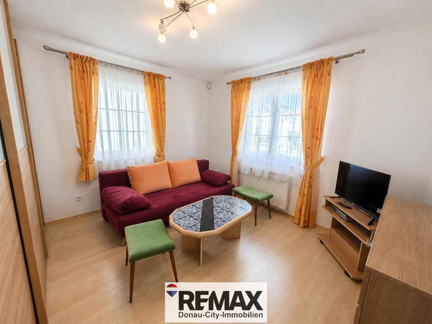 Helles Zimmer mit Laminatboden, rotem Sofa und bunten Vorhängen, ideal als Gästezimmer.