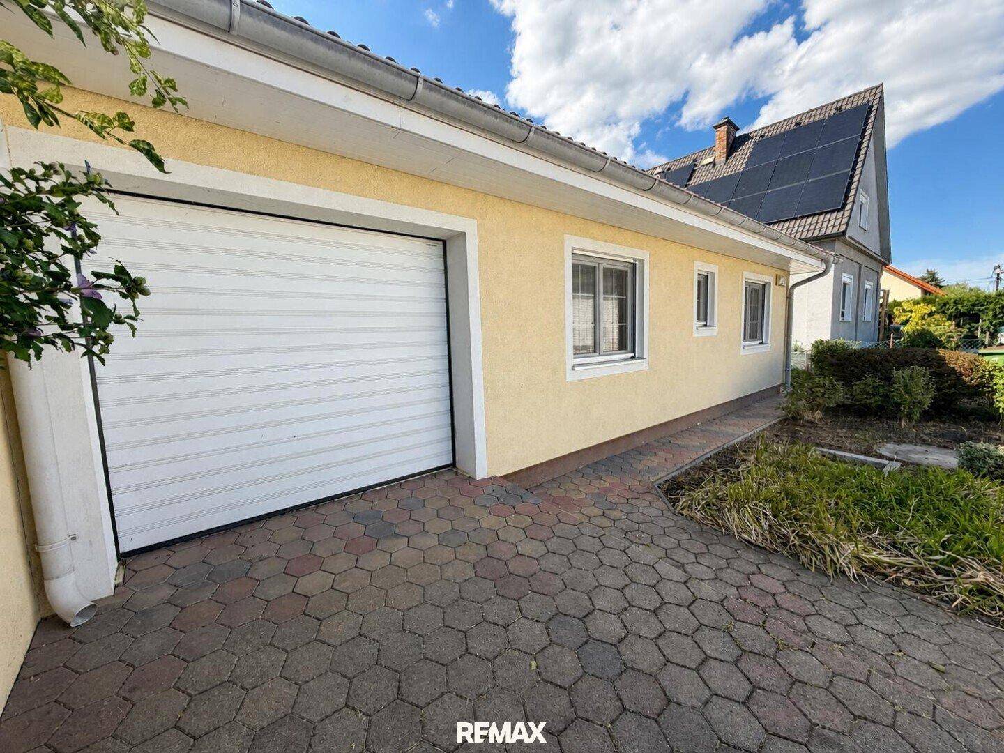 Garagentor und Seitenansicht des Hauses mit gepflasterter Zufahrt und Solaranlage auf dem Dach.