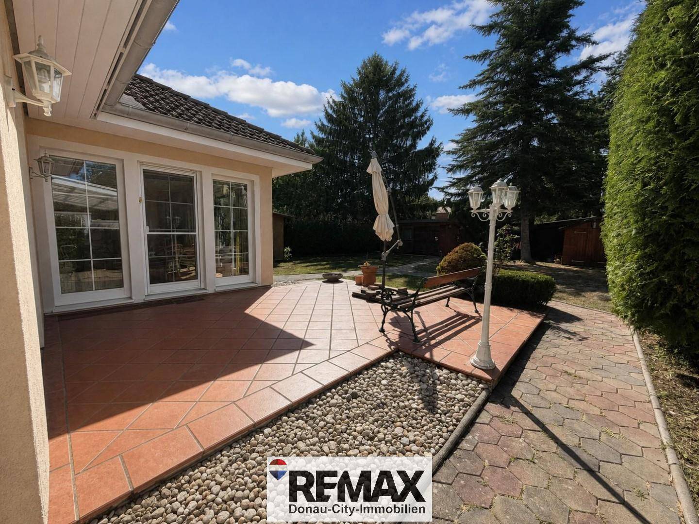 Sonniger Terrassenbereich mit gepflastertem Boden, Sitzbank und Zugang zum Garten.