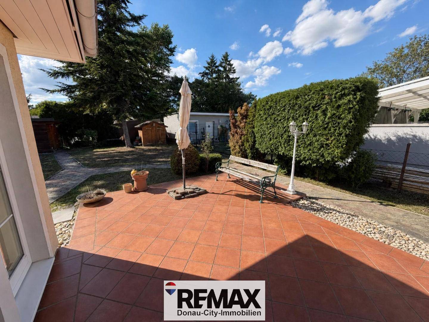 Geräumige Terrasse mit Sitzbank und Sonnenschirm, angrenzend an den Gartenbereich.
