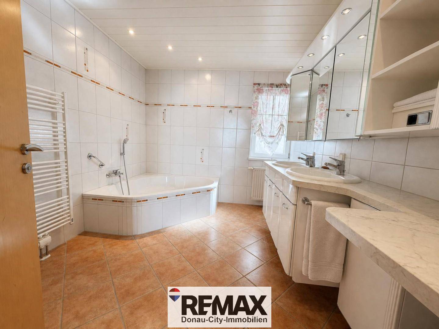 Geräumiges Badezimmer mit Eckbadewanne, Doppelwaschbecken und Fliesenboden.