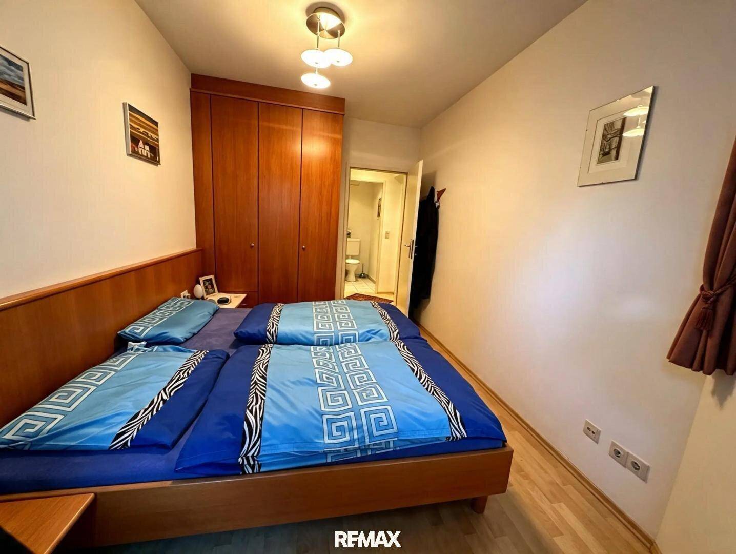 Schlafzimmer mit Doppelbett, Holzschrank und hellem Parkettboden.
