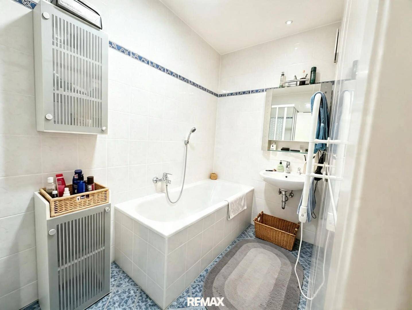 Badezimmer mit Badewanne, Waschbecken und blauen Fliesen im 80er-Jahre-Stil.