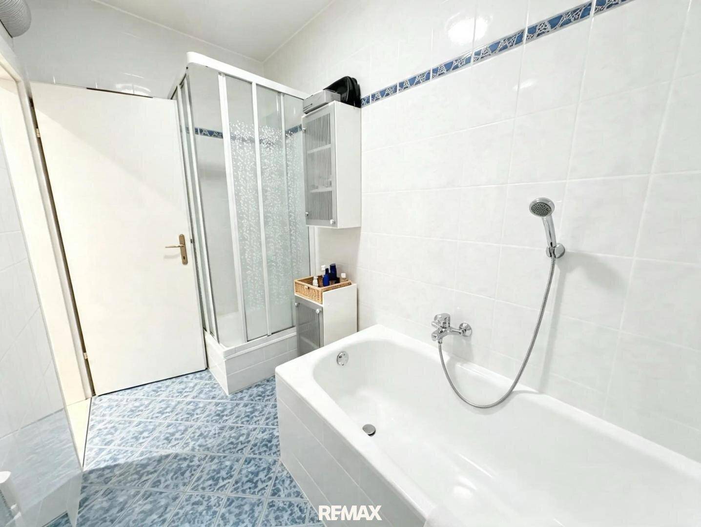 Badezimmer mit Badewanne und Duschkabine, ausgestattet mit blauen Bodenfliesen.