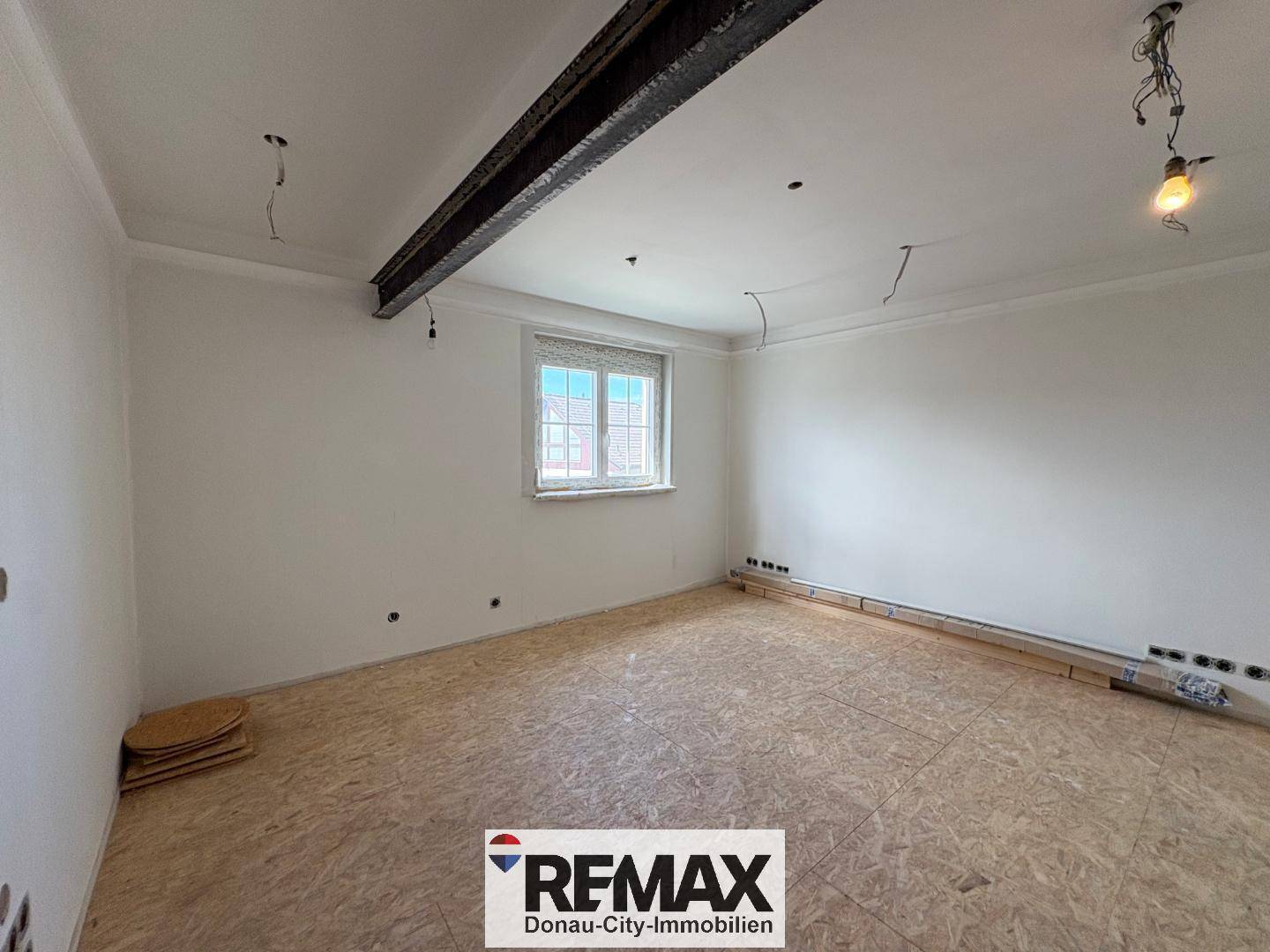 Renovierungsbedürftiger Raum mit OSB-Boden und sichtbaren Deckenbalken, bereit für den Ausbau.