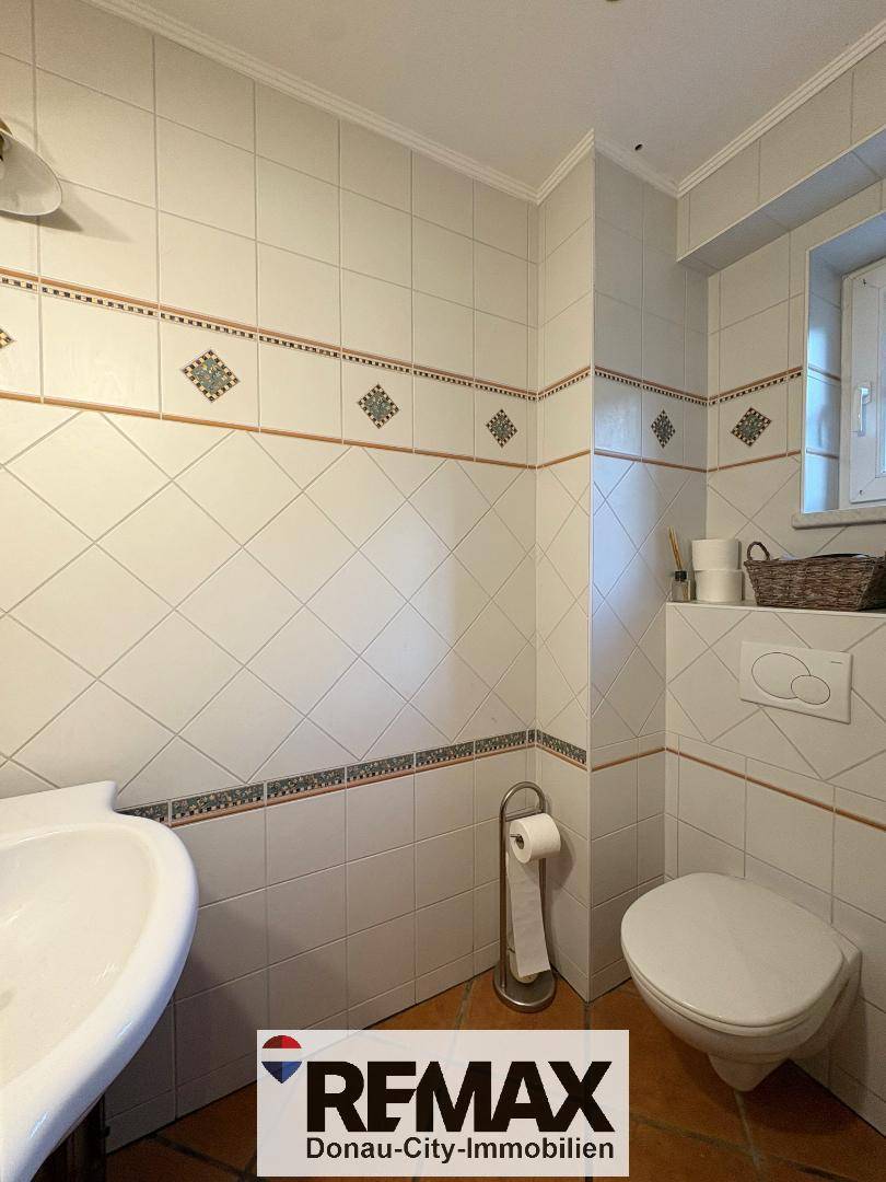 Kleines WC mit weißen Fliesen, Wand-WC und Waschbecken, ausgestattet mit Fenster.