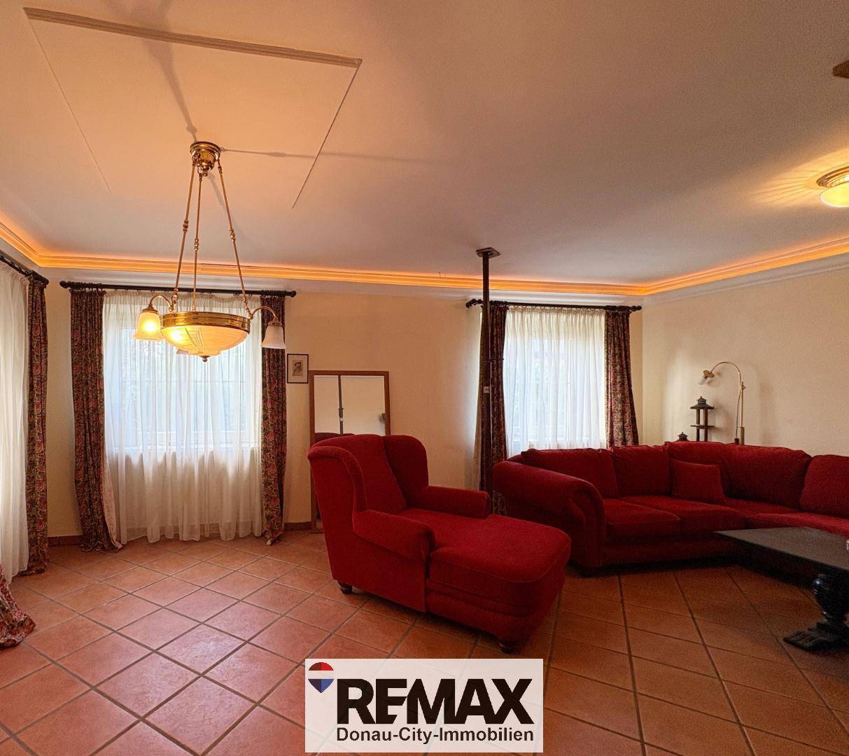 Gemütliches Wohnzimmer mit roten Sofas, Terrakottafliesen und indirekter Deckenbeleuchtung.