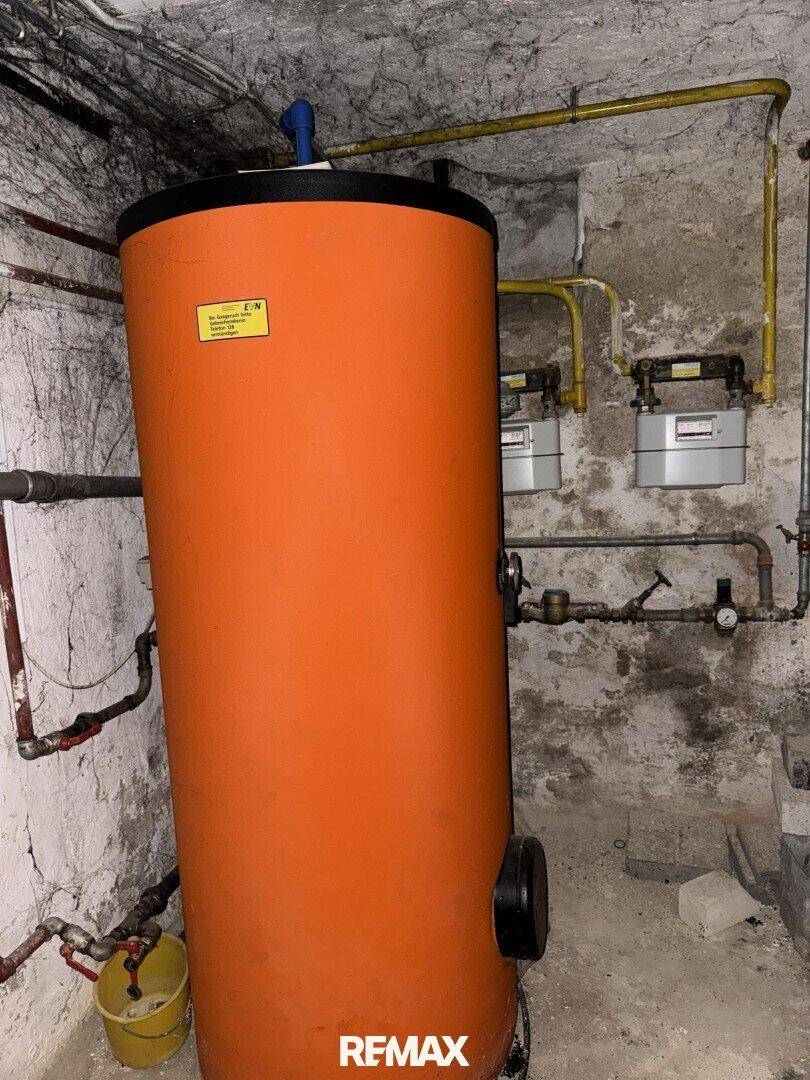 Heizungsraum mit großem Warmwasserspeicher und sichtbaren Rohrleitungen, funktional und geräumig.