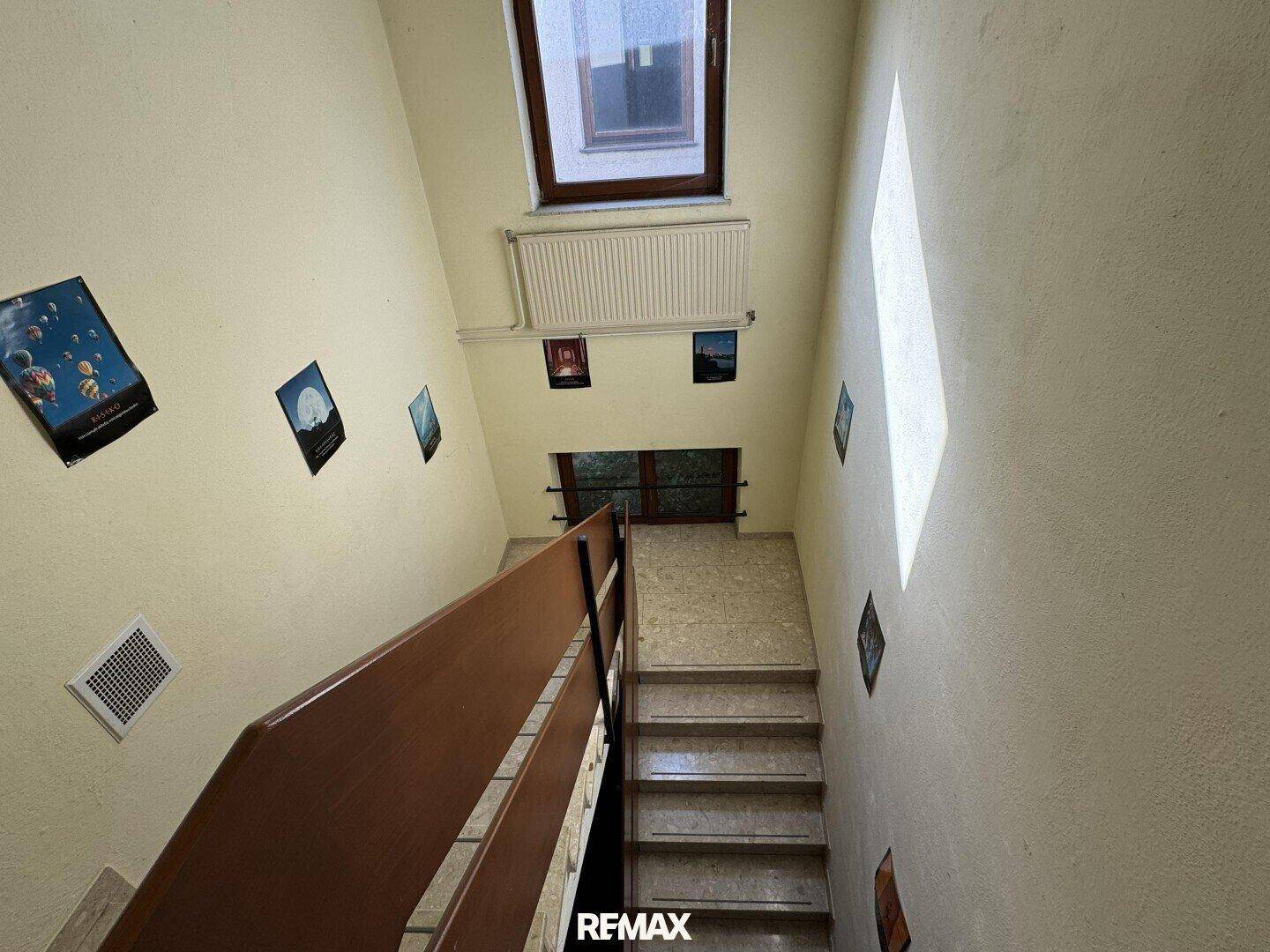 Treppenhaus mit hellem Fliesenboden und einem Fenster, das den Bereich mit Licht versorgt.