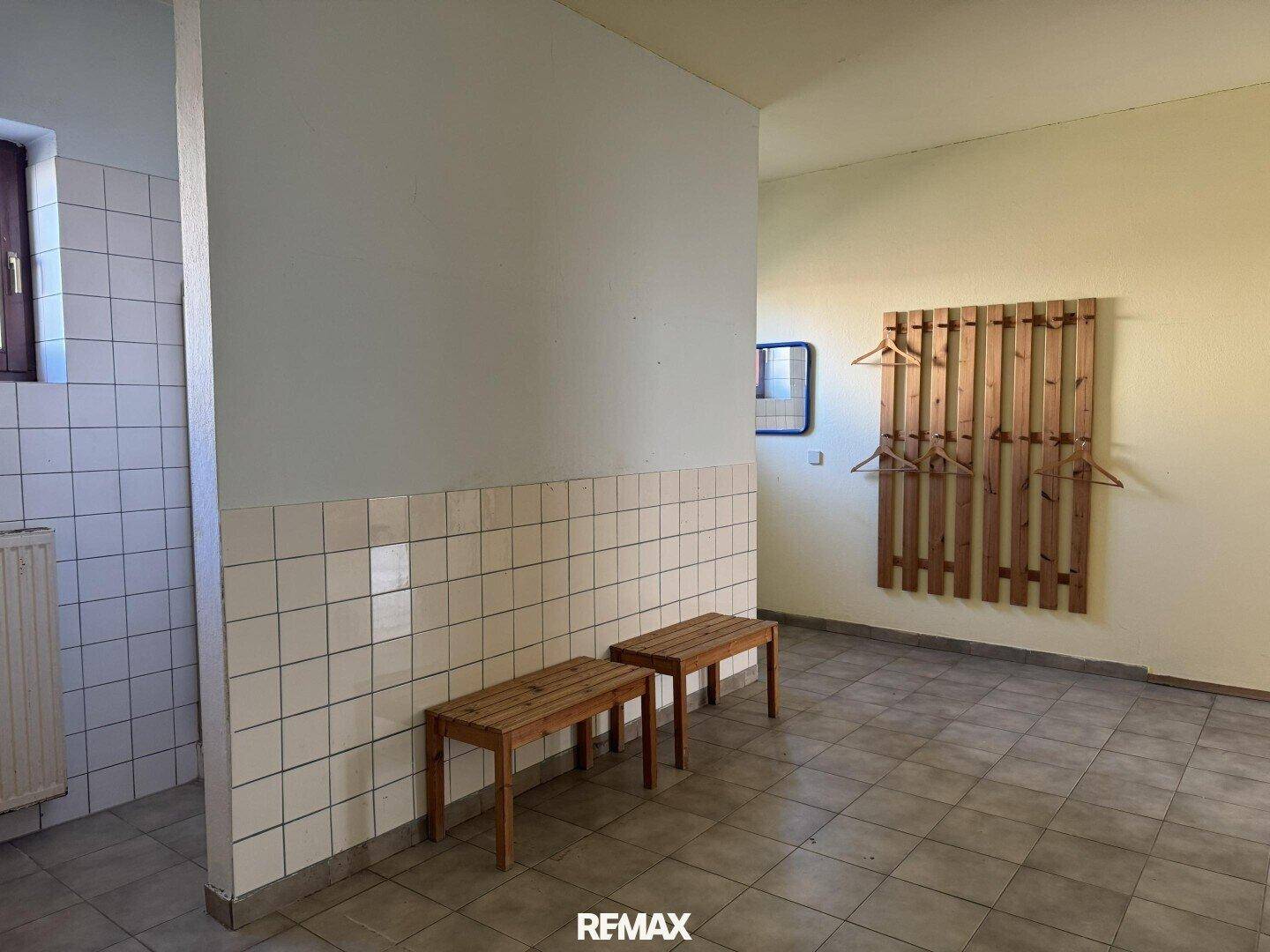 Umkleideraum mit Fliesenboden, Holzbänken und Kleiderhaken, praktisch und funktional.