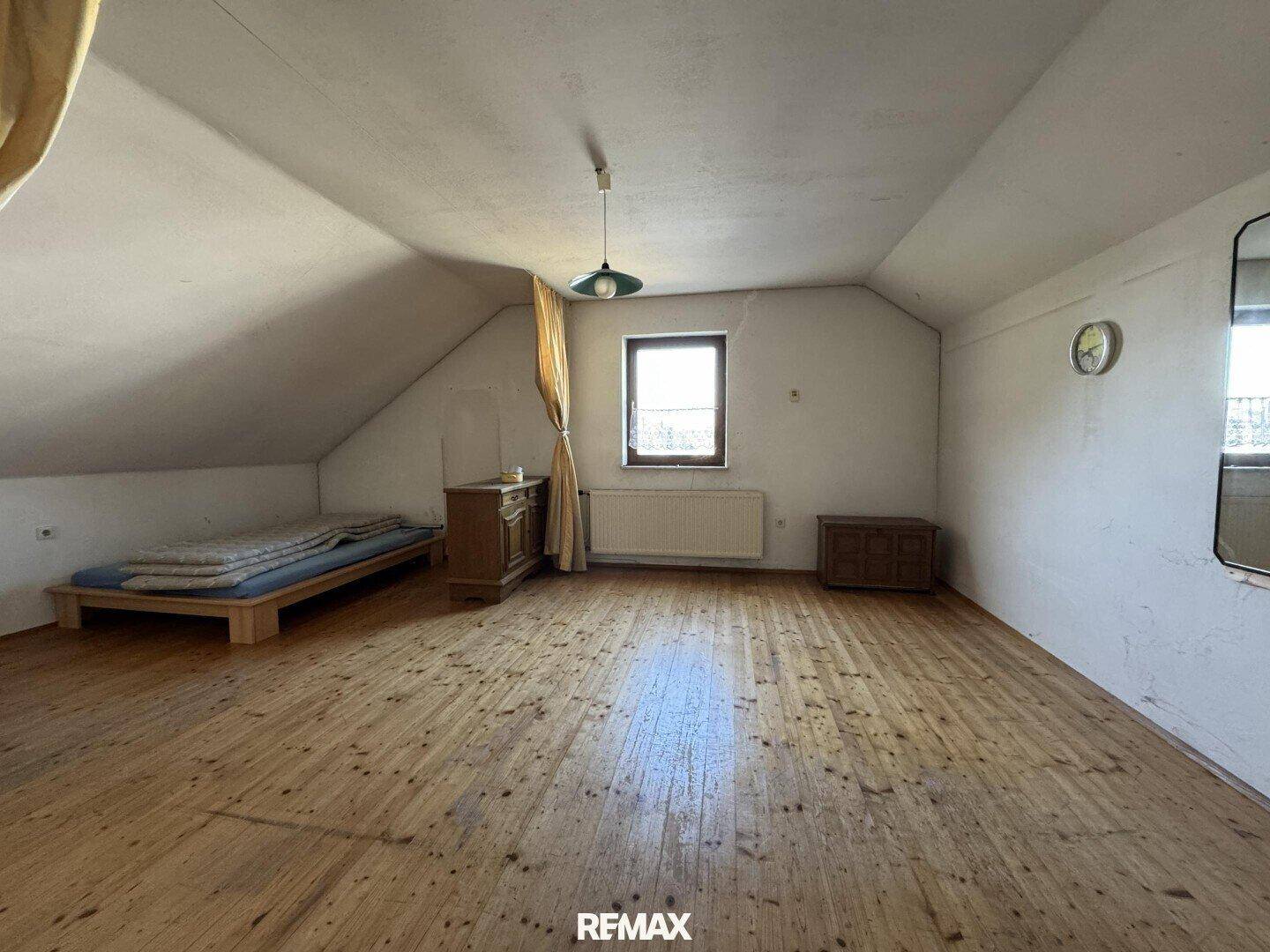 Schlafzimmer im Dachgeschoss mit Holzdielenboden, schräger Decke und einem Fenster für natürliches Licht.