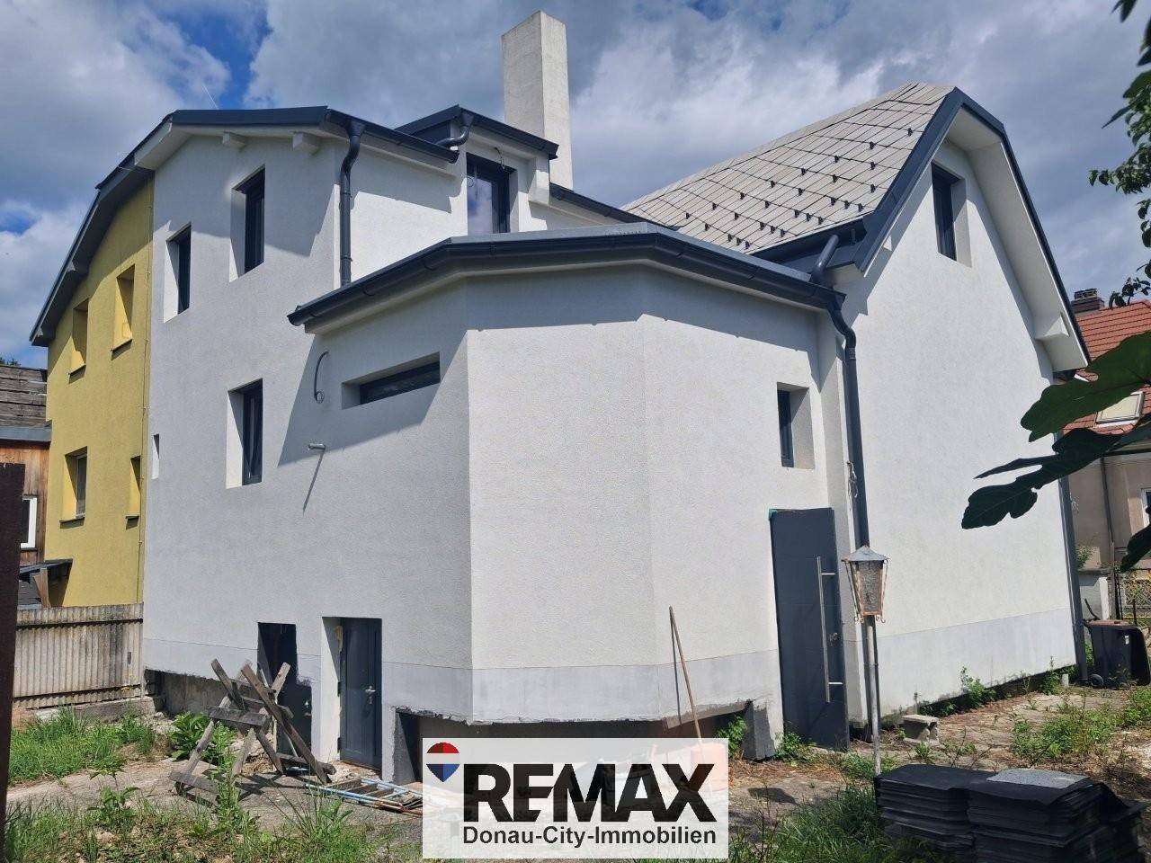 Rückwärtige Ansicht des Hauses mit weißer Fassade und einem Anbau, umgeben von unfertigem Gelände.