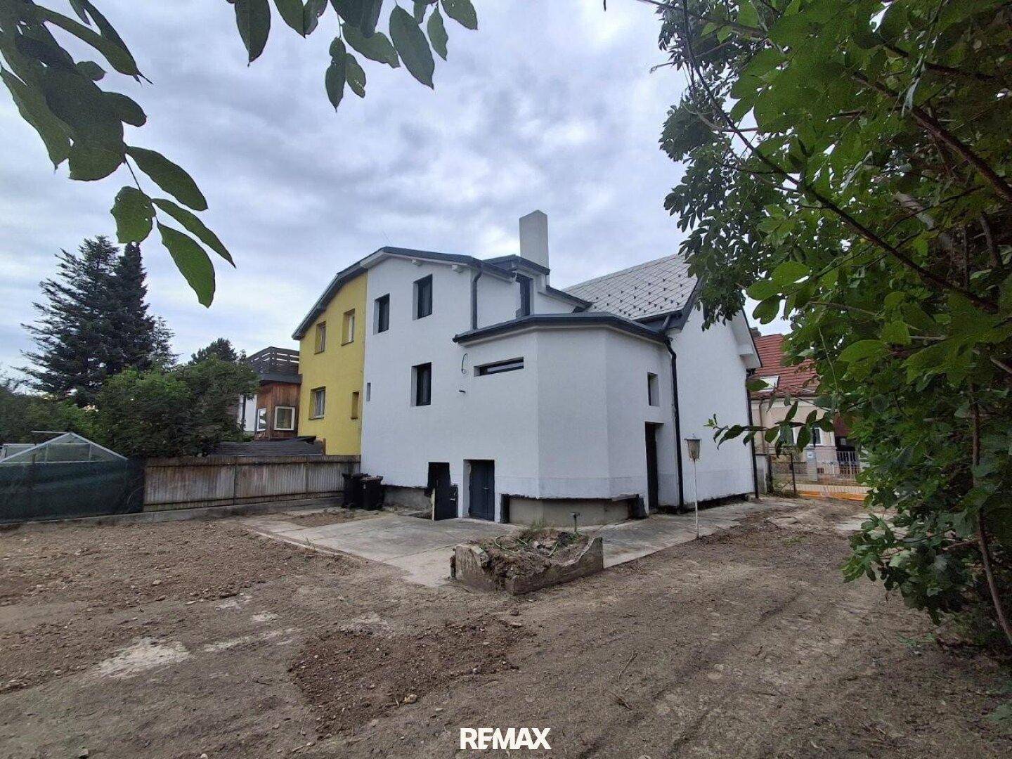 Rückansicht des Hauses mit weißer Fassade und unfertigem Gartenbereich.