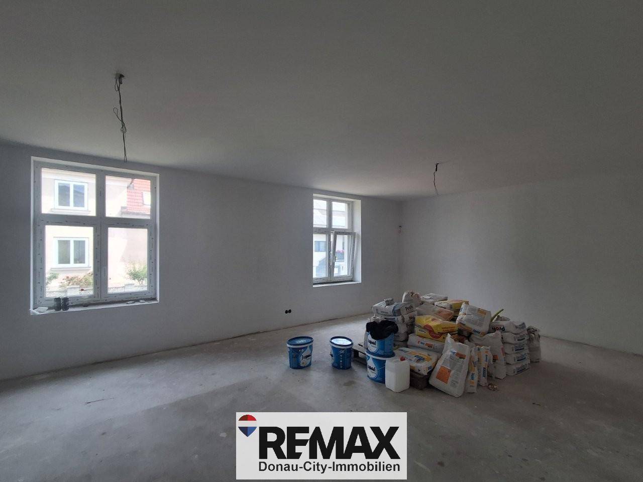Unfertiger Innenraum mit weißen Wänden, Betonboden und Baumaterialien, bereit für den Ausbau.