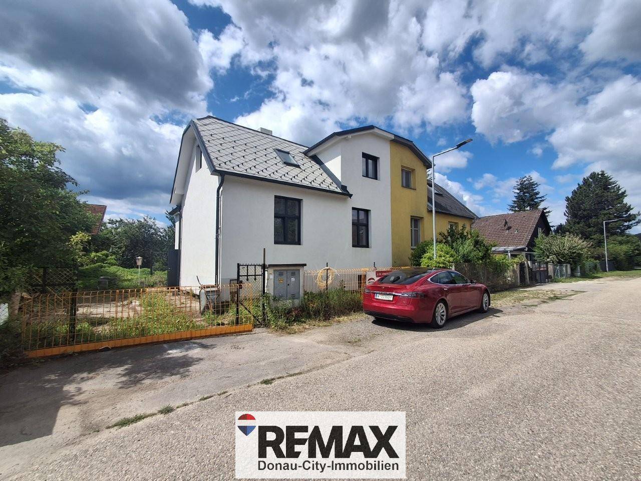 Vorderansicht des Hauses mit weißer Fassade und angrenzendem älteren Teil, geparkt an der Straße.