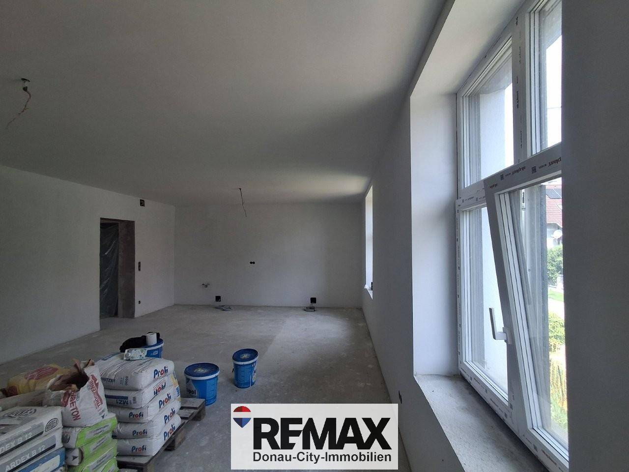 Heller Innenraum im Rohbau mit großen Fenstern und Betonboden, bereit für den Ausbau.