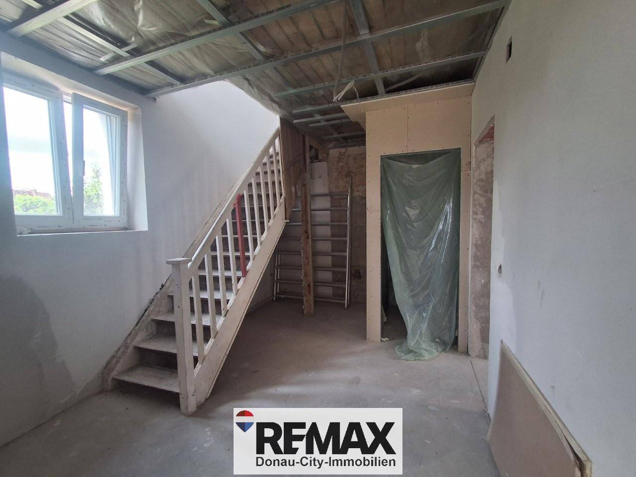 Treppenhaus im Rohbau mit Holztreppe und weißen Wänden, bereit für den weiteren Ausbau.