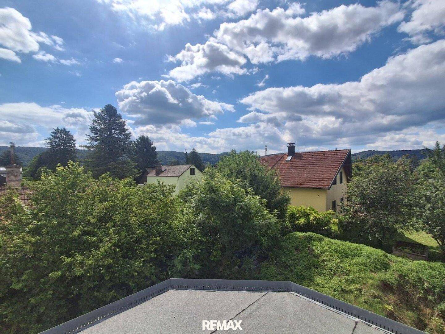 Weitläufiger Blick über grüne Hügel und Dächer von Häusern unter blauem Himmel.