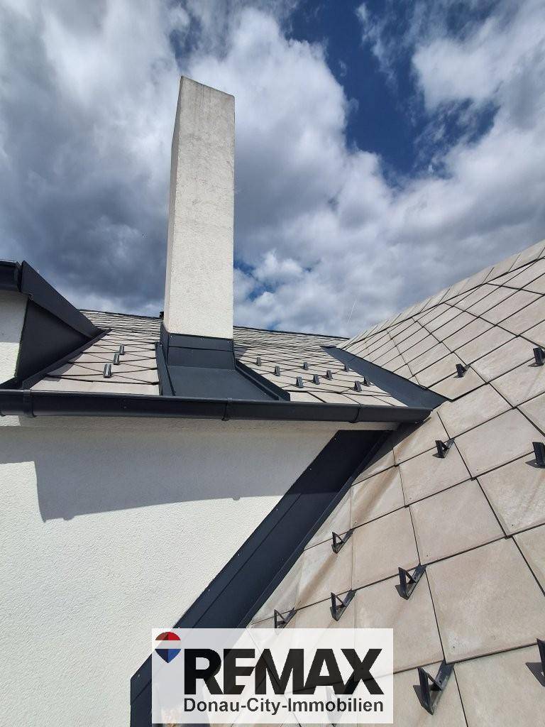 Detailansicht des Daches mit modernen Ziegeln und einem hohen, schlanken Schornstein.